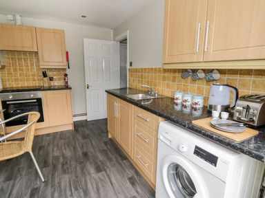 A kitchen with wooden cabinets washing machine toaster kettle and chairs at Byefield Lodge in Welland
