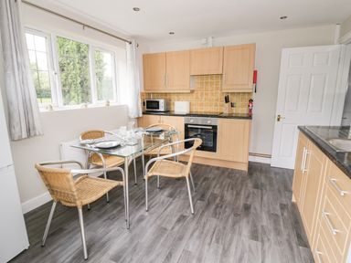 A kitchen with a glass dining table and four wicker chairs at Byefield Lodge in Welland
