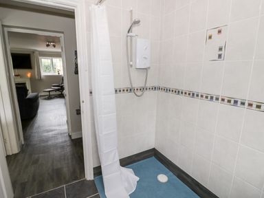 A bathroom shower area with white tiles and blue floor mat next to a doorway leading to a living room at Byefield Lodge in Welland