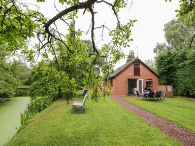 A garden with chairs and a dining table near a brick house by a pond at Byefield Lodge in Welland