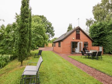 A brick house with an open door and outdoor seating on a lawn with trees and chairs at Byefield Lodge in Welland