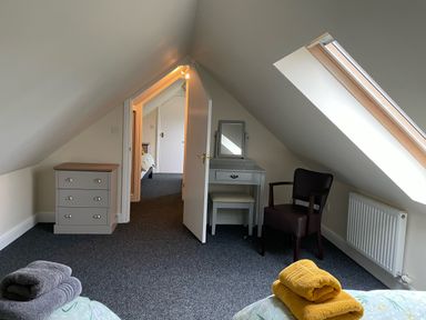 A bedroom with slanted ceiling a chest of drawers a dressing table a chair and folded towels at Byefield Lodge in Welland