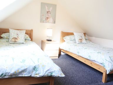 A bedroom with two wooden single beds with floral bedding and rabbit cushions and a nightstand with a lamp at Byefield Lodge in Welland