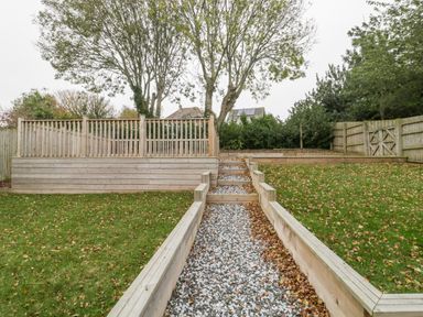 A garden with a gravel path and wooden steps leading to a raised wooden deck and fenced area at Flat 2 38 Preston Road Weymouth