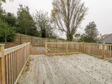 An outdoor wooden deck with a fence and a gate leading to a garden area with trees at Flat 2 38 Preston Road in Weymouth
