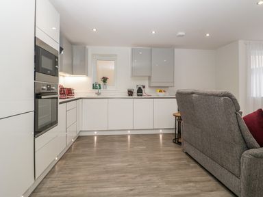 A modern kitchen with white cabinets appliances and a gray sofa at Flat 2 38 Preston Road Weymouth
