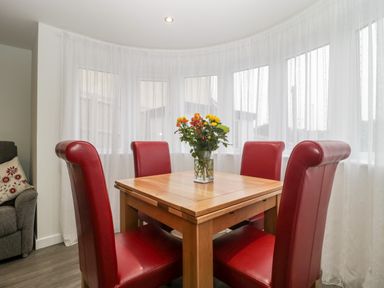 A dining area with a wooden table and four red chairs with a flower vase on the table at Flat 2 38 Preston Road in Weymouth