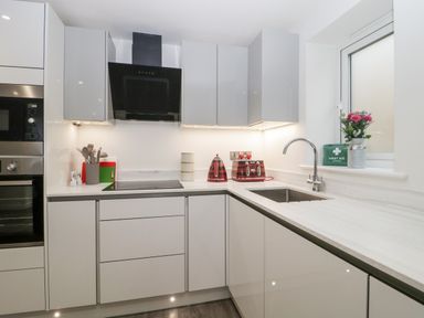 A kitchen with white cabinets a black oven a stovetop a toaster kettle and a sink with a window at Flat 2 38 Preston Road Weymouth