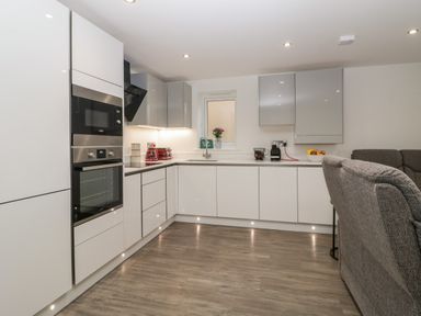 A kitchen with white cabinets built in oven microwave toaster and coffee machine next to a gray sofa at Flat 2 38 Preston Road in Weymouth