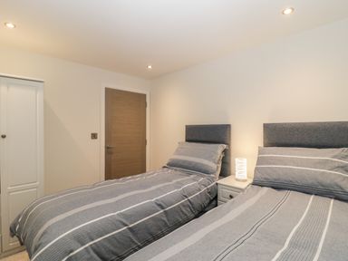 A bedroom with two single beds a nightstand with a lamp a wooden door and a white closet at Flat 2 38 Preston Road in Weymouth