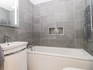 A bathroom with a white bathtub and sink and gray tiled walls at Flat 2 38 Preston Road in Weymouth