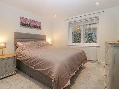 A bedroom with a double bed, two bedside tables with lamps, a chest of drawers, and a window at Flat 2, 38 Preston Road in Weymouth