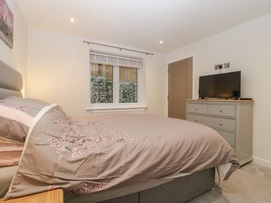 A bedroom with a bed with floral bedding a chest of drawers with a TV on top a window and a door at Flat 2 38 Preston Road in Weymouth