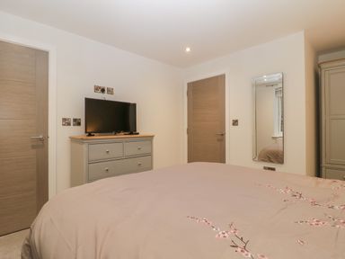 A bedroom with a bed with patterned bedspread a dresser with a television a wall mirror and two wooden doors at Flat 2 38 Preston Road in Weymouth