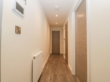 A hallway with wooden flooring white walls a radiator and three closed wooden doors at Flat 2 38 Preston Road Weymouth