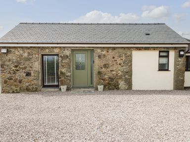 A stone and white exterior wall with a green door and two windows at Tyddyn Haidd in Amlwch