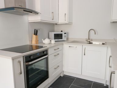 A kitchen with white cabinets a built-in oven a microwave a sink a cutting board and knives at Tyddyn Haidd in Amlwch