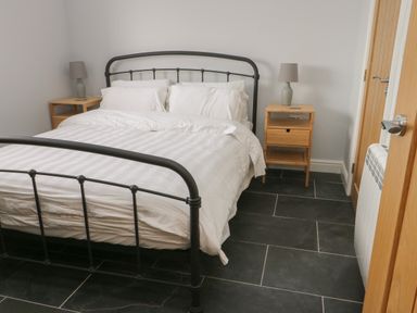 A bedroom with a black metal bed frame white bedding two wooden bedside tables with lamps and a closed wooden door at Tyddyn Haidd in Amlwch