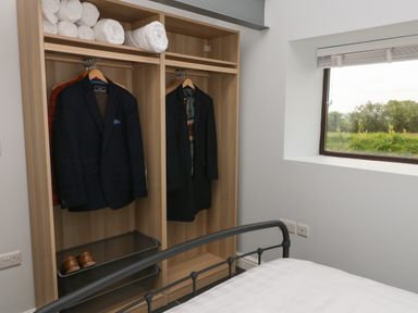 A bedroom with an open wardrobe containing jackets towels and shoes next to a window at Tyddyn Haidd in Amlwch