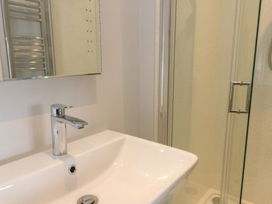 A bathroom sink with a chrome faucet and a glass shower door at Tyddyn Haidd in Amlwch