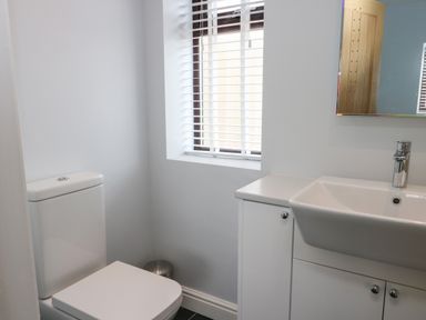 A bathroom with a toilet, a sink with cabinet, a window with blinds, and a mirror at Tyddyn Haidd in Amlwch