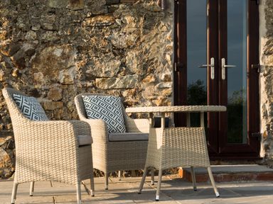 A stone wall with two wicker chairs and a wicker table on a tiled patio at Tyddyn Haidd in Amlwch