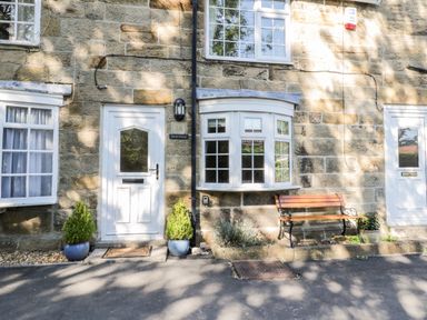 A stone facade with a white door and window beside a wooden bench and potted plants at Parva in Great Broughton near Stokesley