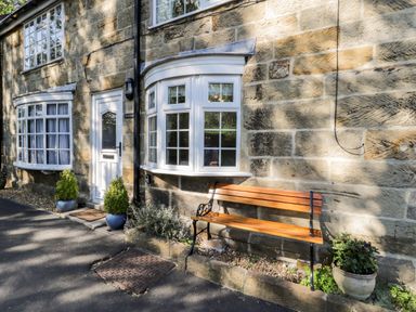 A stone house exterior with white framed windows a white door two potted plants and a wooden bench at Parva in Great Broughton near Stokesley