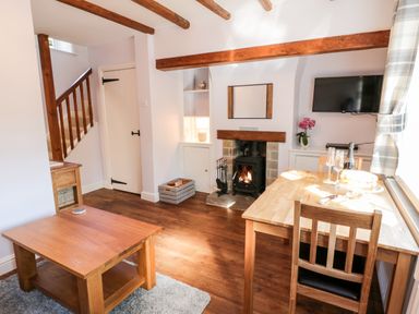 A sitting area with wooden beams and a wood burning stove and a dining table by a window at Parva in Great Broughton near Stokesley