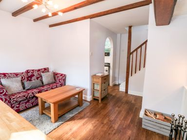 A living room with a red patterned sofa a wooden coffee table a small wooden cabinet and visible stairs at Parva Great Broughton near Stokesley