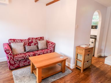 A living room with a red patterned sofa wooden coffee table and a small wooden storage unit near an arched doorway at Parva in Great Broughton near Stokesley