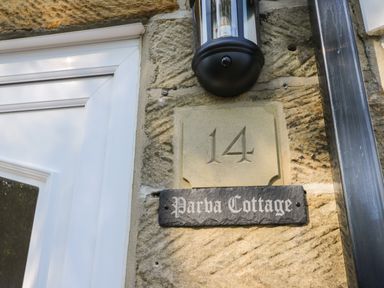 A house number 14 and a sign saying Parva Cottage on a stone wall next to a white door and a black outdoor light at Parva Cottage in Great Broughton near Stokesley