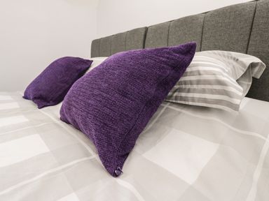 A bed with gray headboard two purple pillows and striped bedsheets at Parva in Great Broughton near Stokesley