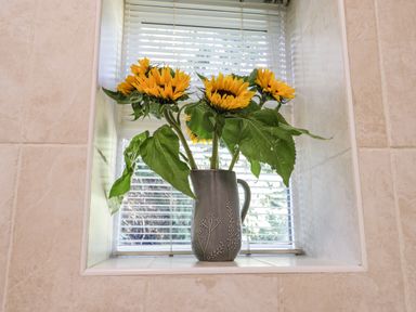 A vase with sunflowers on a tiled window sill with white blinds at Parva Great Broughton near Stokesley