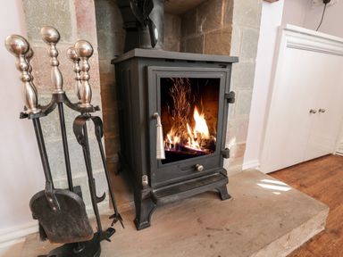 A wood burning stove with fire inside and fireplace tools on a stone hearth at Parva in Great Broughton near Stokesley