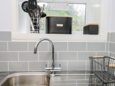 A kitchen sink with a chrome faucet and utensil holder on the window sill and a metal dish rack on the counter at Parva Great Broughton near Stokesley