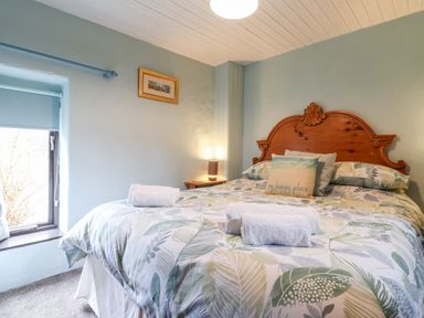 A bedroom with a wooden headboard bed with leaf patterned bedding and a blue wall at Barn Court Cottage Narberth Pembrokeshire