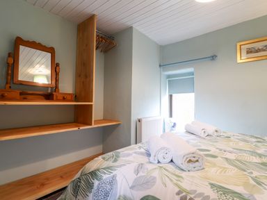 A bedroom with a bed with rolled towels on it a wooden shelf with a mirror and hangers and a window at Barn Court Cottage Narberth Pembrokeshire