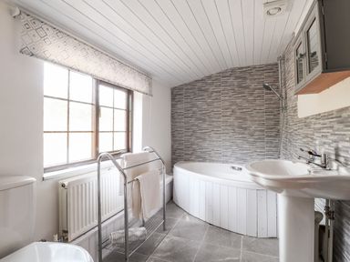 A bathroom with a window towel rack corner bathtub sink and toilet at Barn Court Cottage Narberth Pembrokeshire