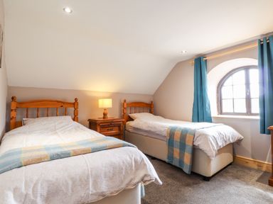 A bedroom with two single beds a wooden nightstand with a lamp and a window with blue curtains at Barn Court Cottage in Narberth Pembrokeshire