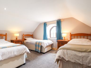 A bedroom with three single beds two wooden bedside tables and a window with blue curtains at Barn Court Cottage Narberth Pembrokeshire