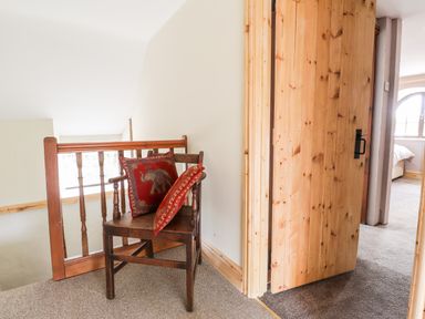 A wooden chair with two red cushions near a wooden banister and an open wooden door leading to a bedroom at Barn Court Cottage in Narberth Pembrokeshire