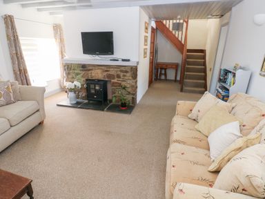 A living room with two sofas a stone fireplace with a stove and a wall-mounted tv near stairs and a bookshelf at Barn Court Cottage Narberth Pembrokeshire