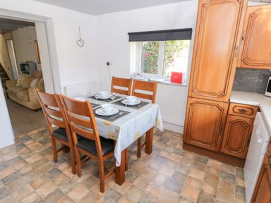 A dining area with a wooden table and four chairs set with dishes and glasses next to wooden kitchen cabinets and a window at Barn Court Cottage in Narberth Pembrokeshire