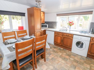 A kitchen with wooden cabinets a dining table set for four a washing machine and dishwasher at Barn Court Cottage Narberth Pembrokeshire
