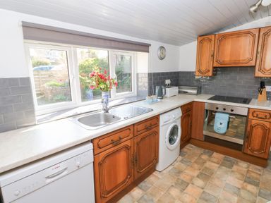 A kitchen with wooden cabinets a sink dishwasher oven washing machine and a window with flowers on the sill at Barn Court Cottage Narberth Pembrokeshire