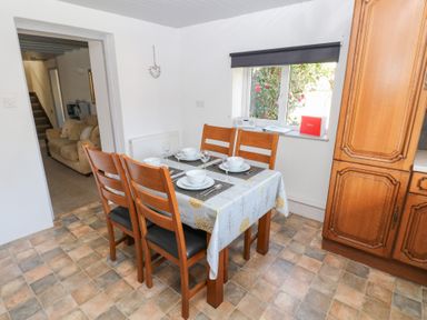 A dining area with a table set for four near a window and wooden cabinets at Barn Court Cottage in Narberth Pembrokeshire