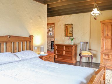 A bedroom with a wooden bed a dresser a chair and a mirror at Stoney Cottage in Narberth Pembrokeshire