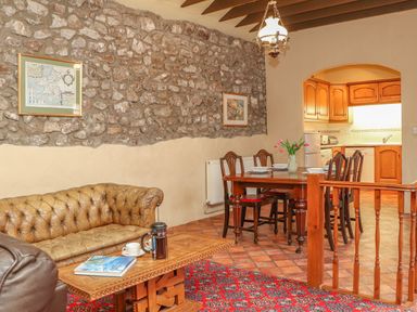 A dining area with wooden table and chairs next to a kitchen with wooden cabinets and a living area with a leather sofa and wooden coffee table at Stoney Cottage in Narberth Pembrokeshire
