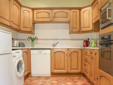 A kitchen with wooden cabinets a washing machine dishwasher refrigerator kettle and oven at Stoney Cottage Narberth Pembrokeshire